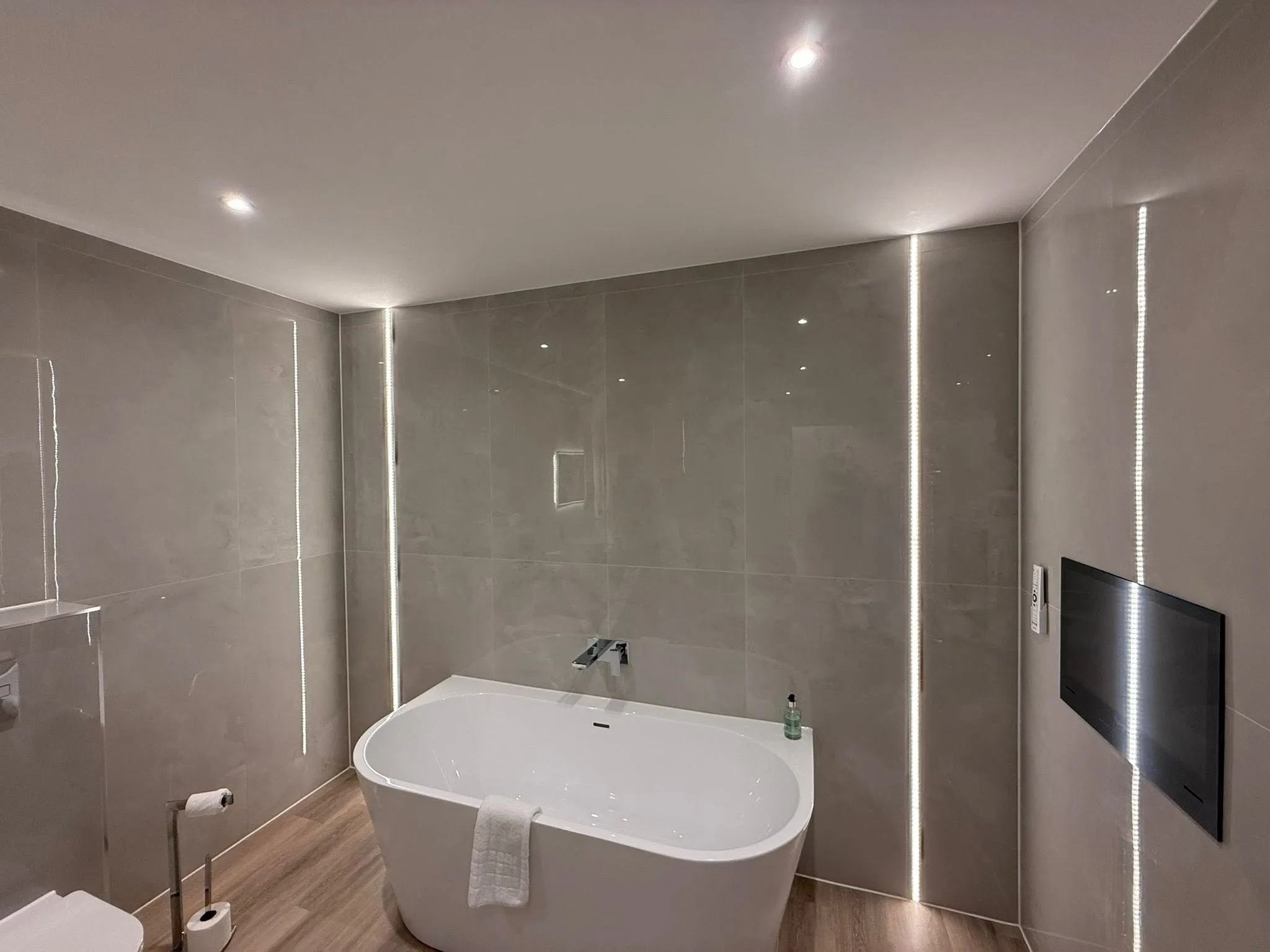 Modern bathroom installation with a freestanding bath, large format tiles and LED lighting