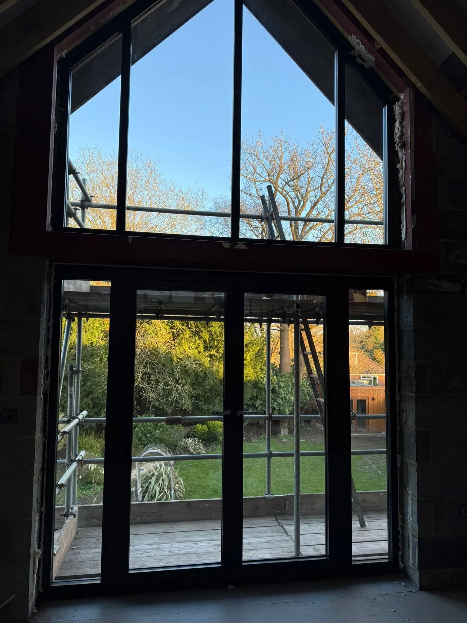 Black aluminium apex window above glazed doors, looking out over the garden from an unfinished room