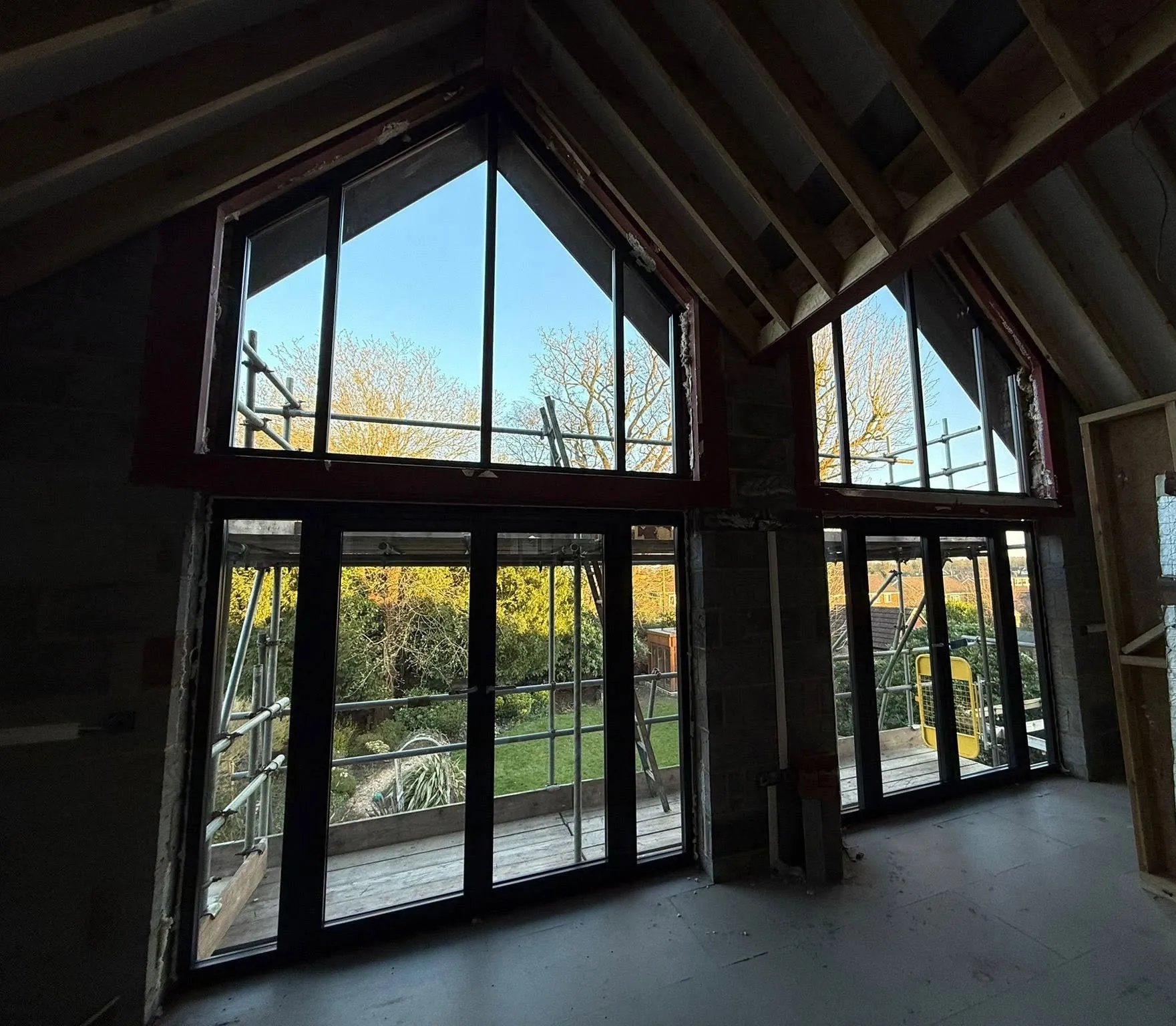 Vaulted room under construction, with two black aluminium apex windows above two sets of glazed doors