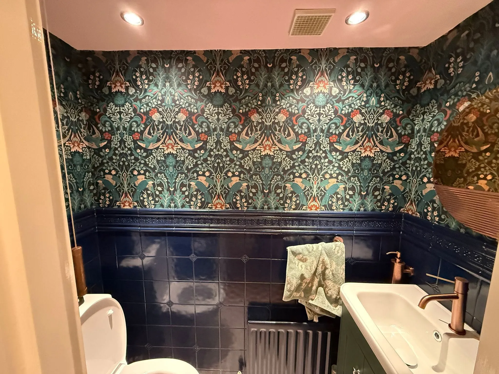Downstairs WC with patterned wallpaper, navy tiling and copper brassware