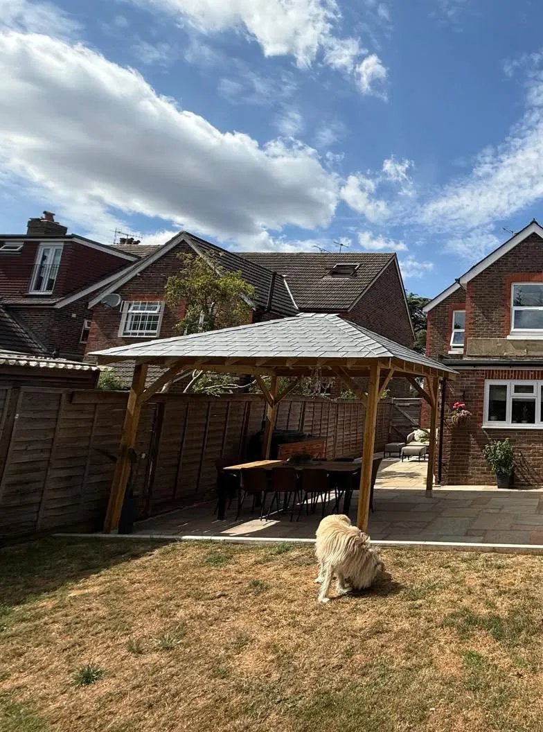 Timber pergola and sandstone patio seen from the lawn, with a dog in the foreground