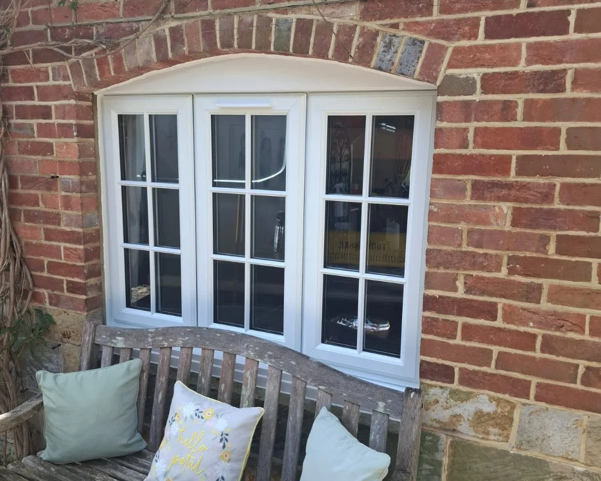 White window with Georgian bars in an arched brick opening, above a weathered garden bench