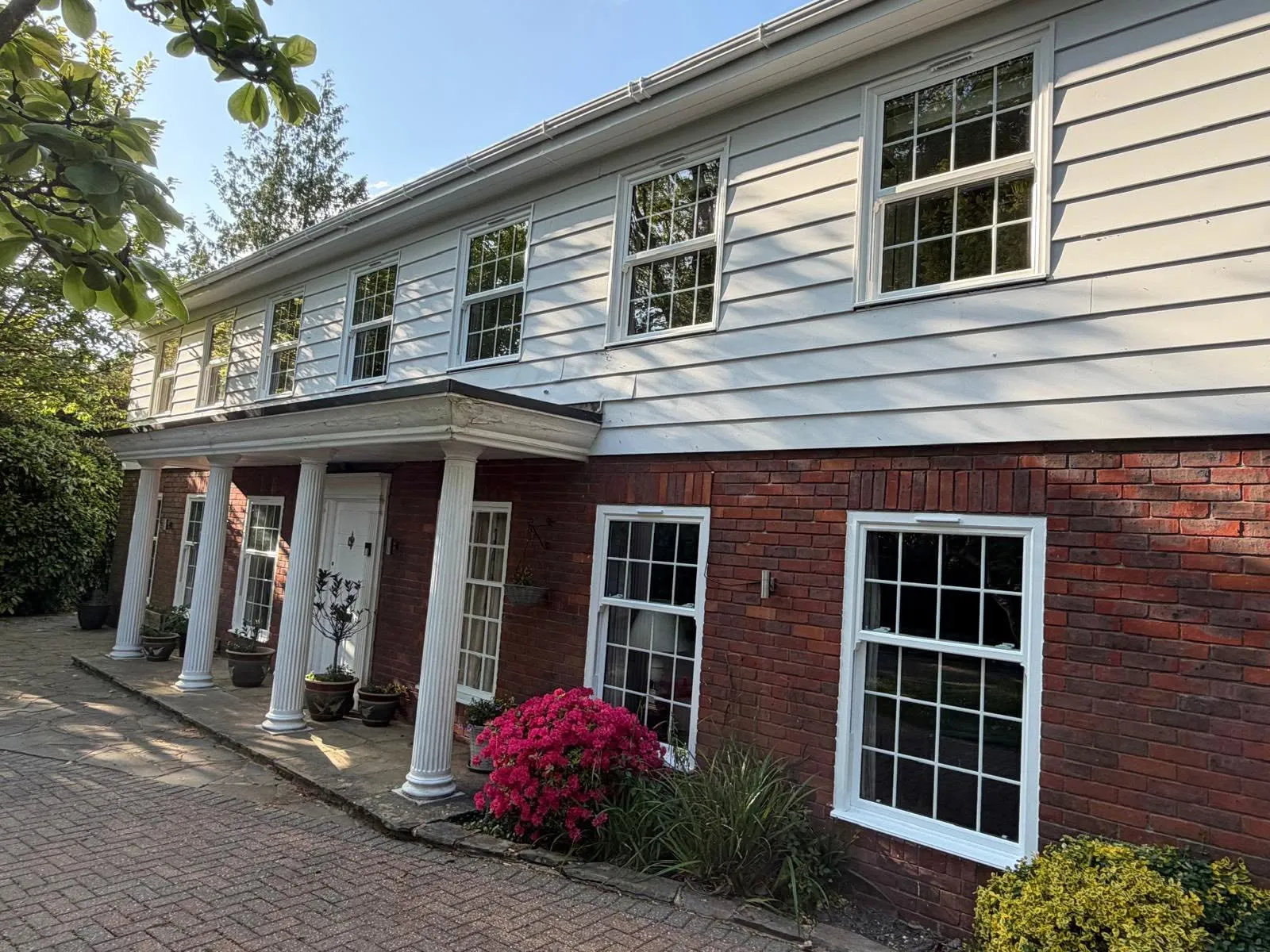 The front of the house at an angle, showing white sash windows with Georgian bars set in brick and white weatherboarding