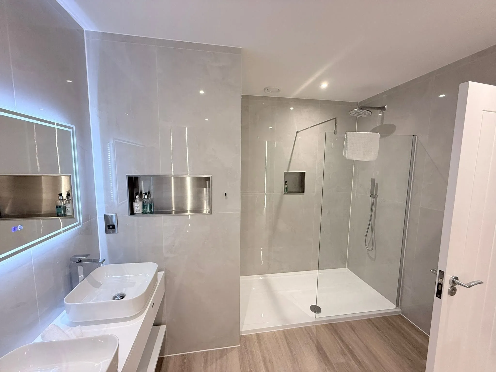 Countertop basins and a backlit mirror, with a walk-in shower beyond