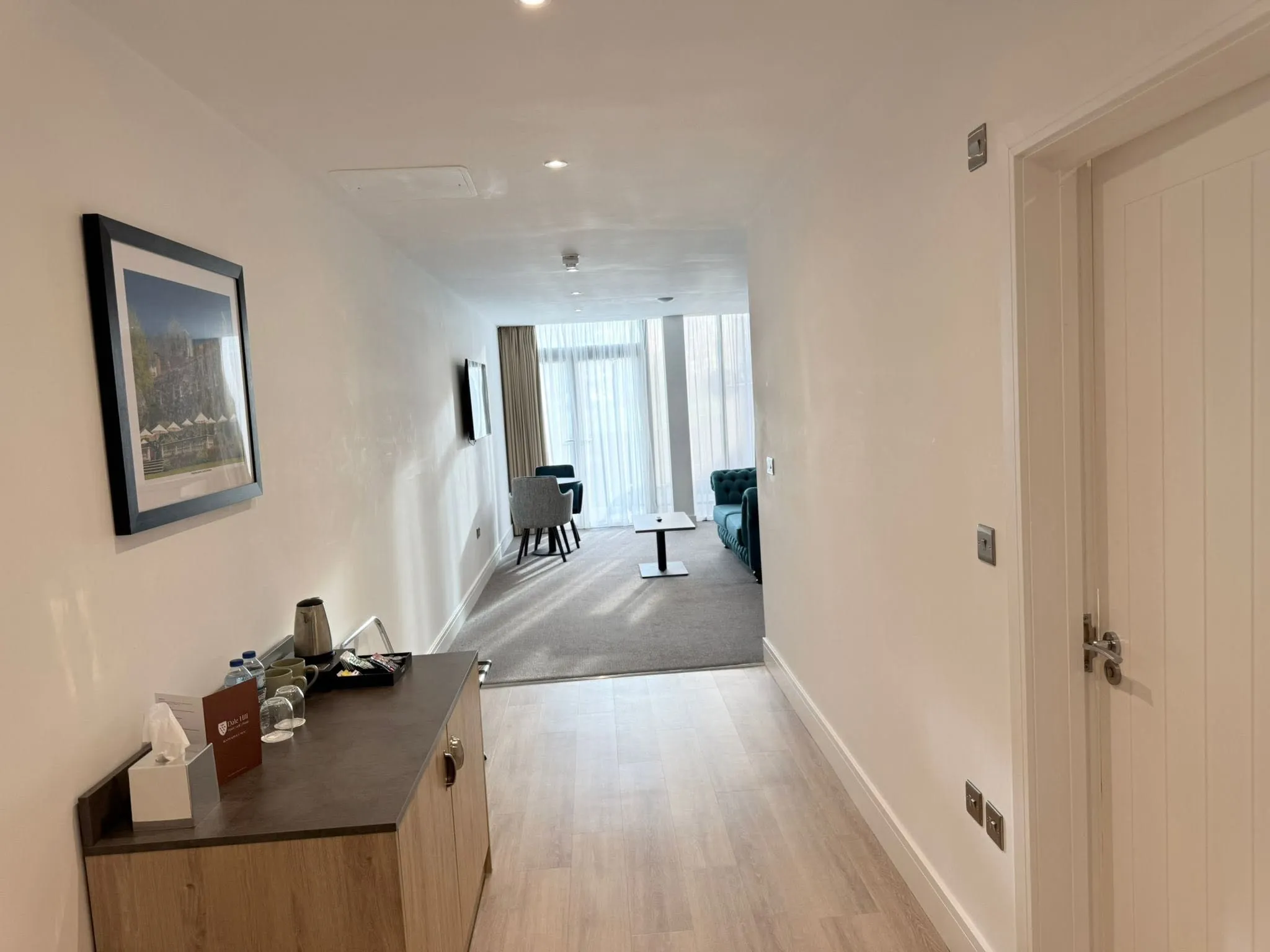 Suite entrance hall with wood-effect flooring and a white panelled door, looking through to the seating area