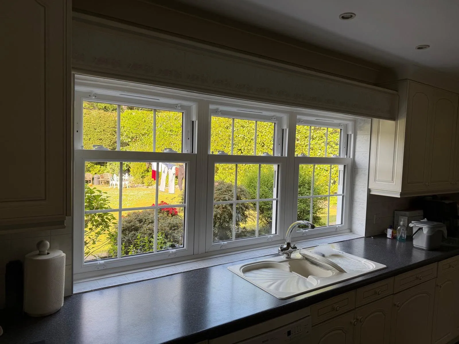 Three white sash windows with Georgian bars side by side above a kitchen sink, looking out to the garden