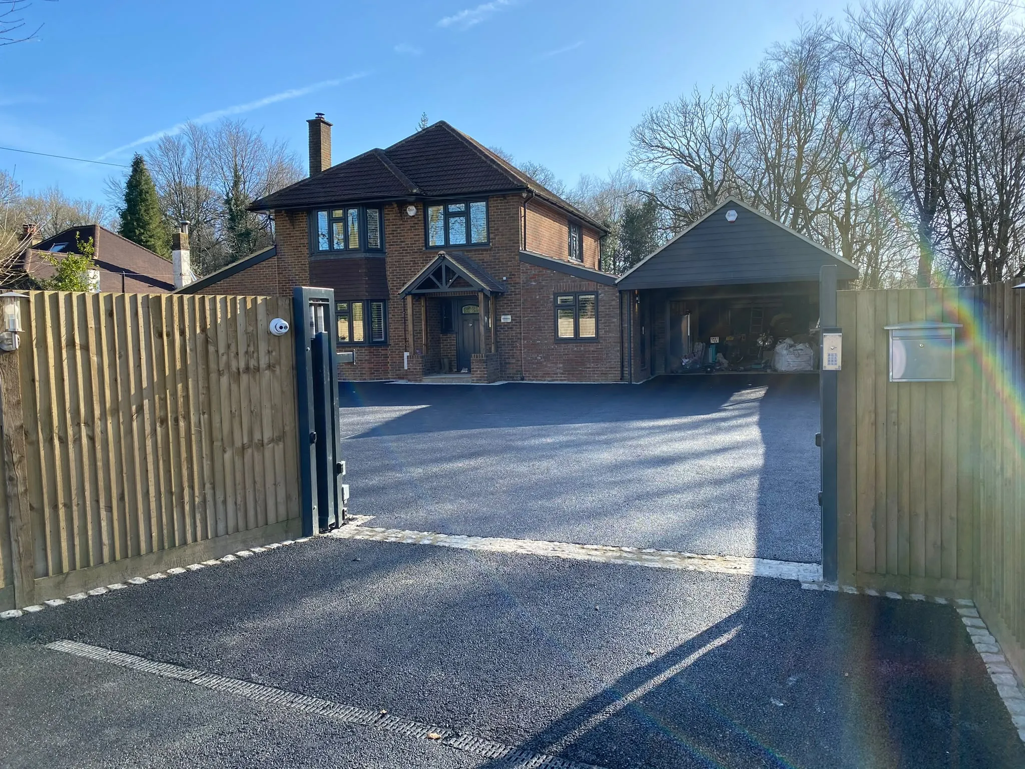 New tarmac driveway with a granite sett edge and timber electric gates, in front of a brick home